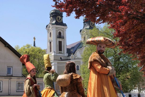 Bunt kostümierte Stelzenläufer vor der Kulisse des Stadtplatzes., © Allgäu GmbH